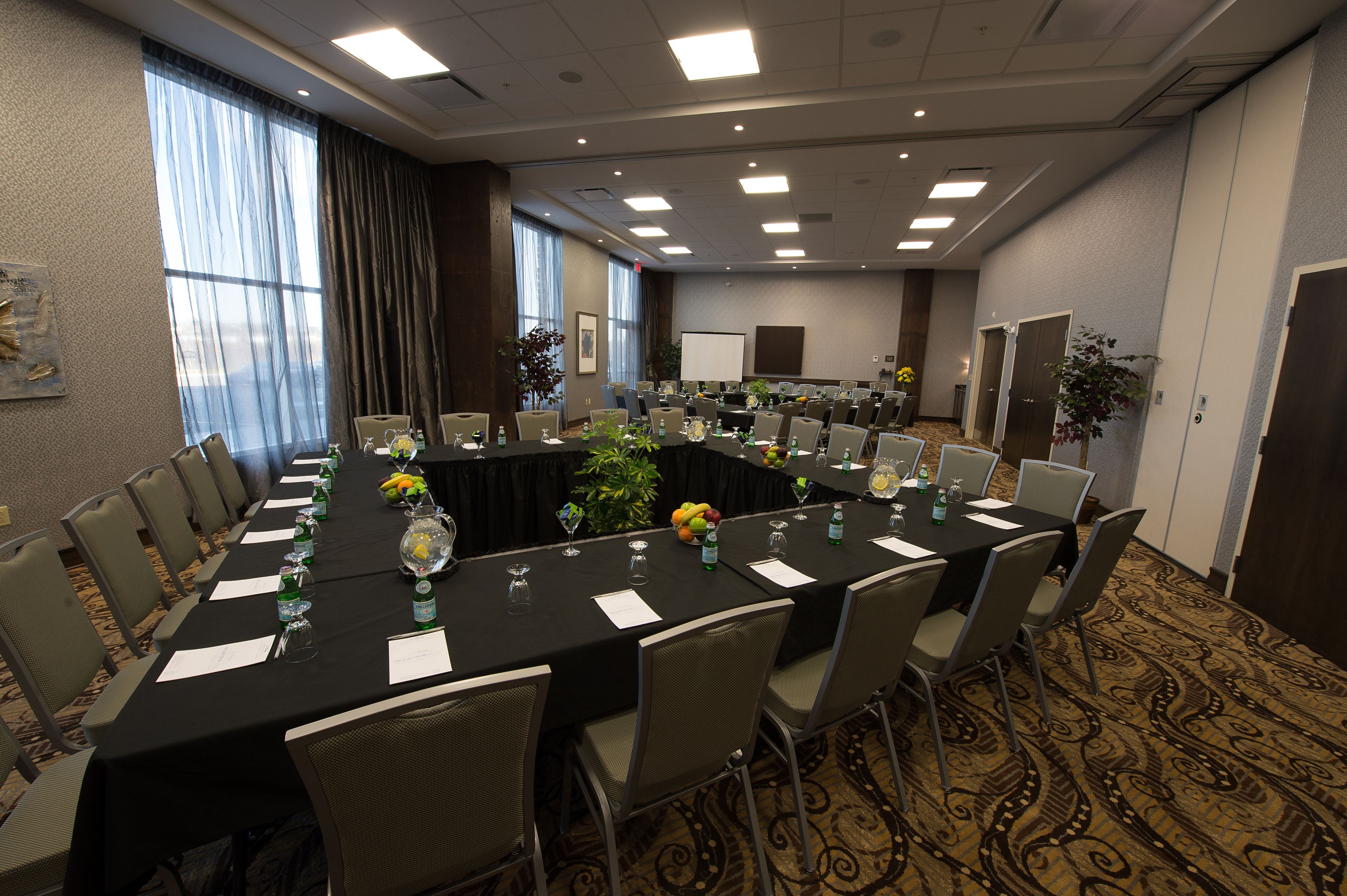 A conference room with a long table, chairs, and a projector screen.