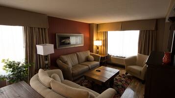 Ein Hotelzimmer mit einer Couch, einem Sessel und einem Couchtisch. Eine Lampe, eine Pflanze und ein Gemälde sind an der Wand zu sehen.