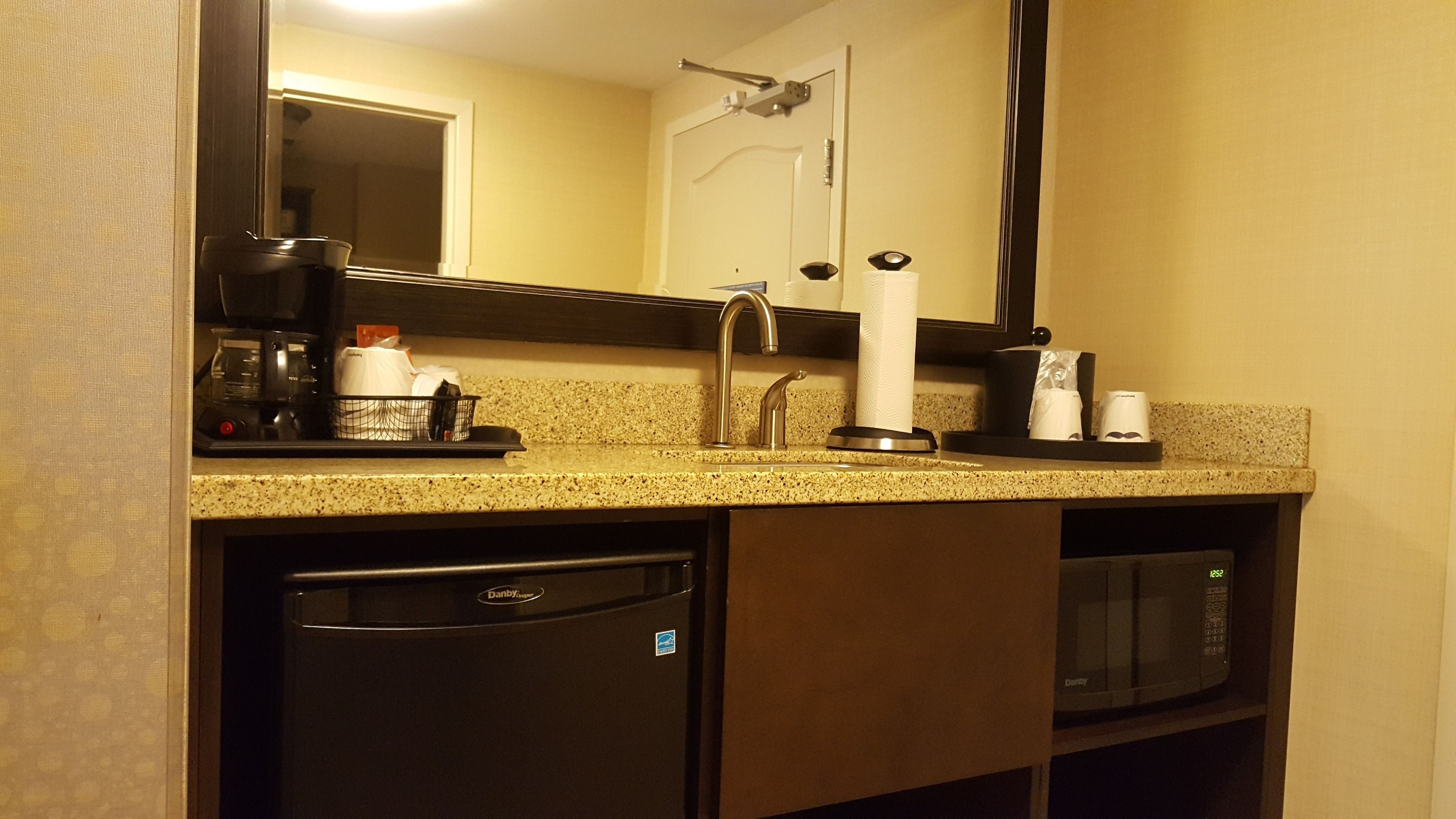 Una cocina pequeña con cafetera, dispensador de toallas de papel y microondas.