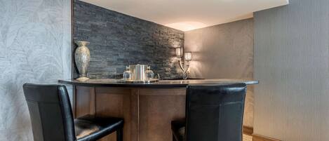 Una cocina moderna con un salpicadero de piedra oscura, dos taburetes de cuero negro y un lavamanos de acero inoxidable.