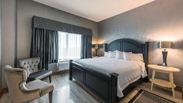 Quarto de hotel com cama grande, uma cadeira, mesa de cabeceira e luminária.