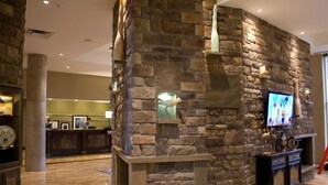 A lobby with a stone wall, a reception desk, and a television. - Hampton Inn by Hilton Sydney (Sydney)