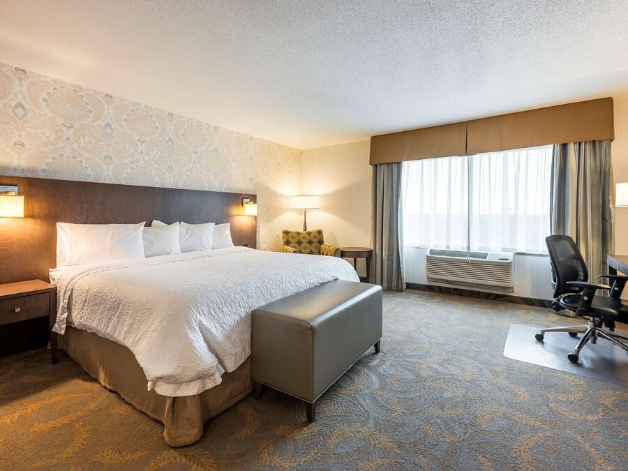 Una habitación de hotel con una cama grande, un escritorio, una silla, una lámpara y una ventana con cortinas.