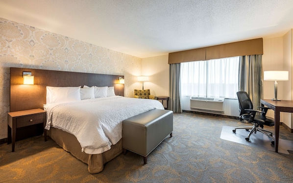Una habitación de hotel con una cama grande, un escritorio, una silla, una lámpara y una ventana con cortinas.