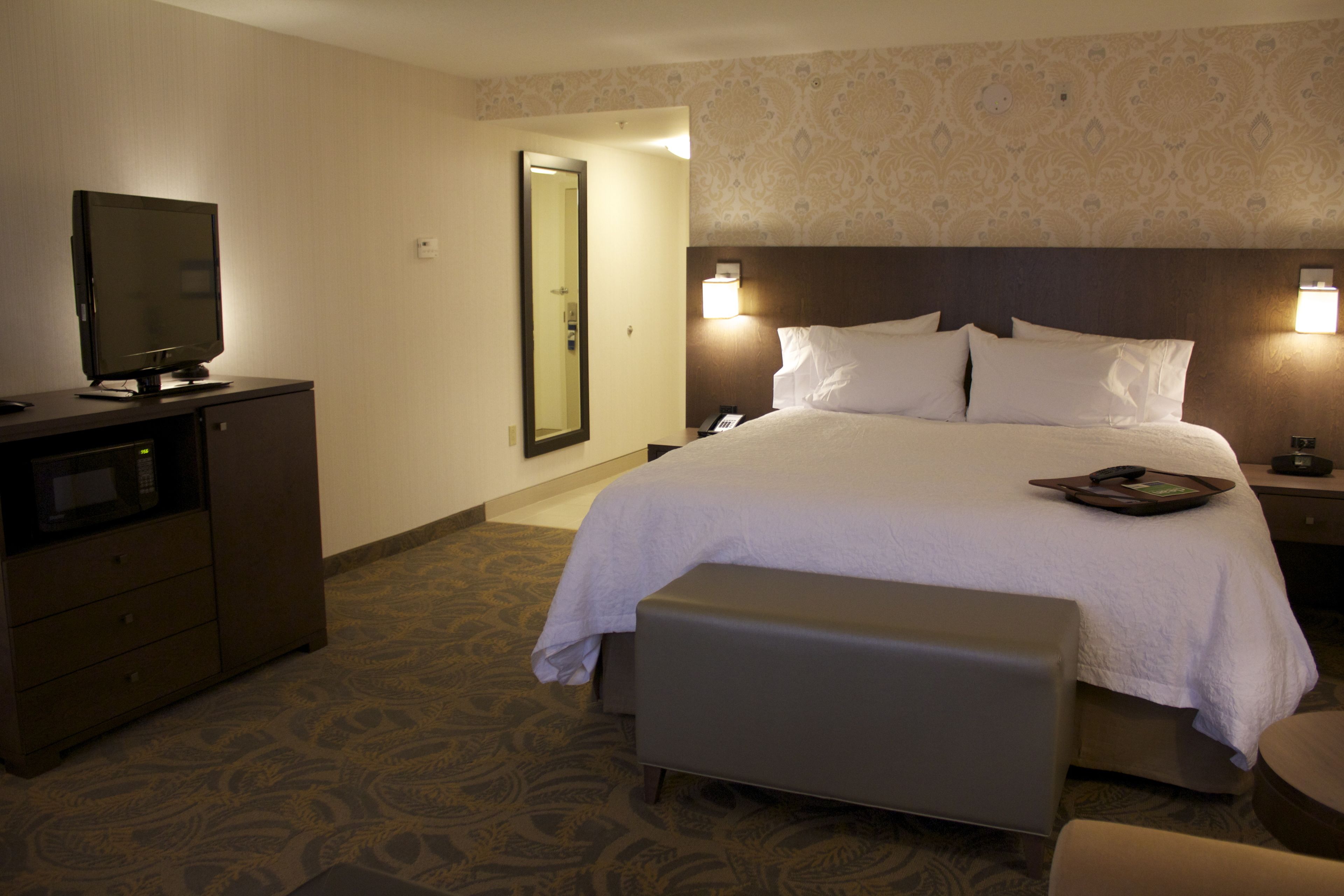 A hotel room with a bed, a television, a desk, and a bench.