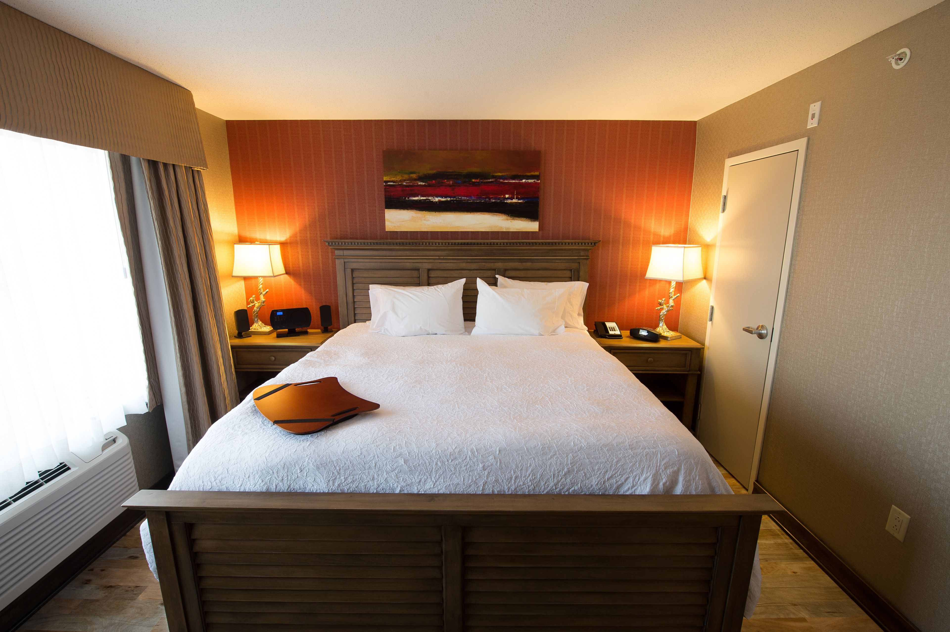 Habitación de hotel con una cama grande, dos mesitas de noche con lámparas, un cuadro sobre la cama y una puerta a la derecha.