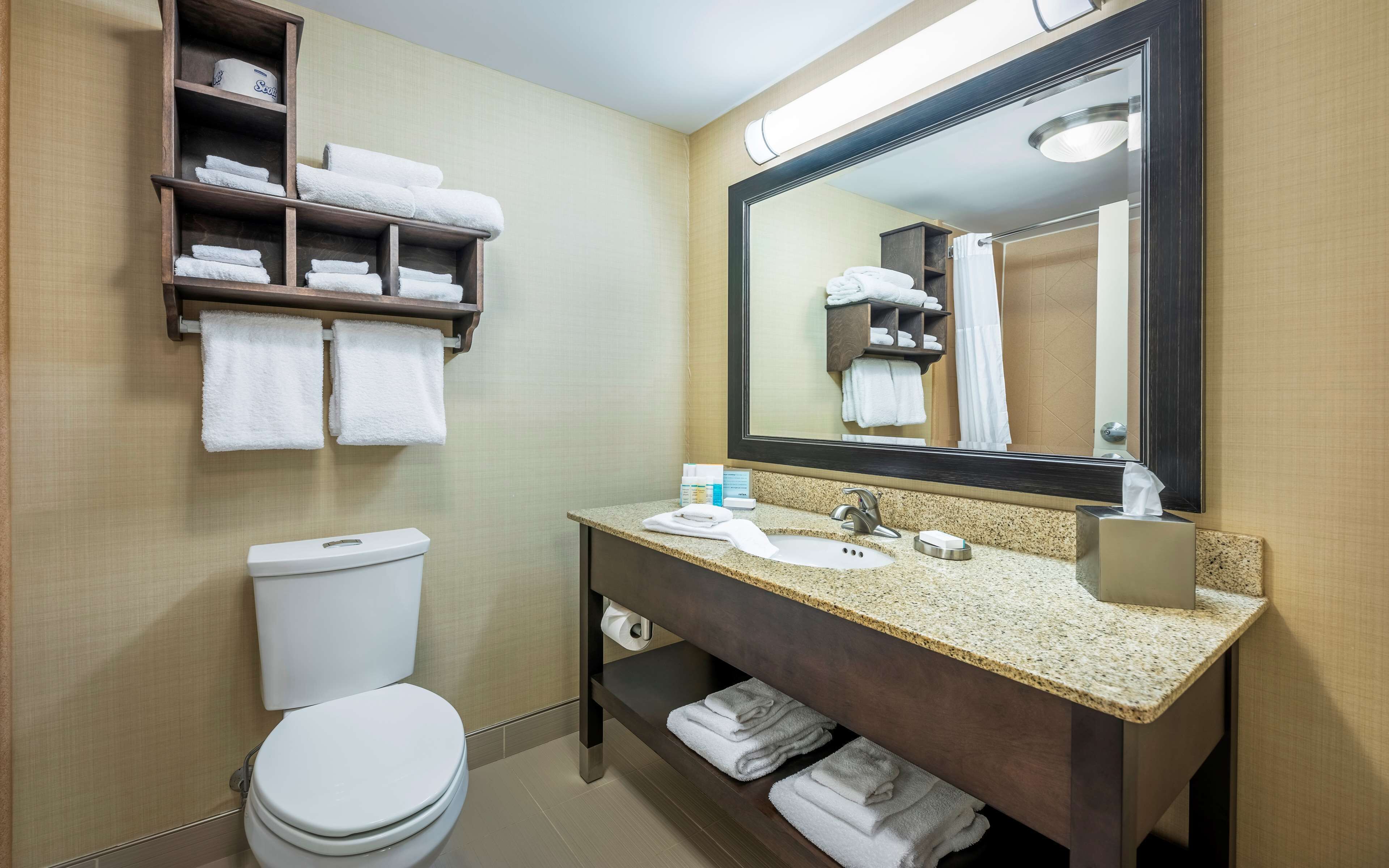 Ein Badezimmer mit Toilette, Waschbecken, Spiegel, Handtuchhalter und Regalen mit Handtüchern.