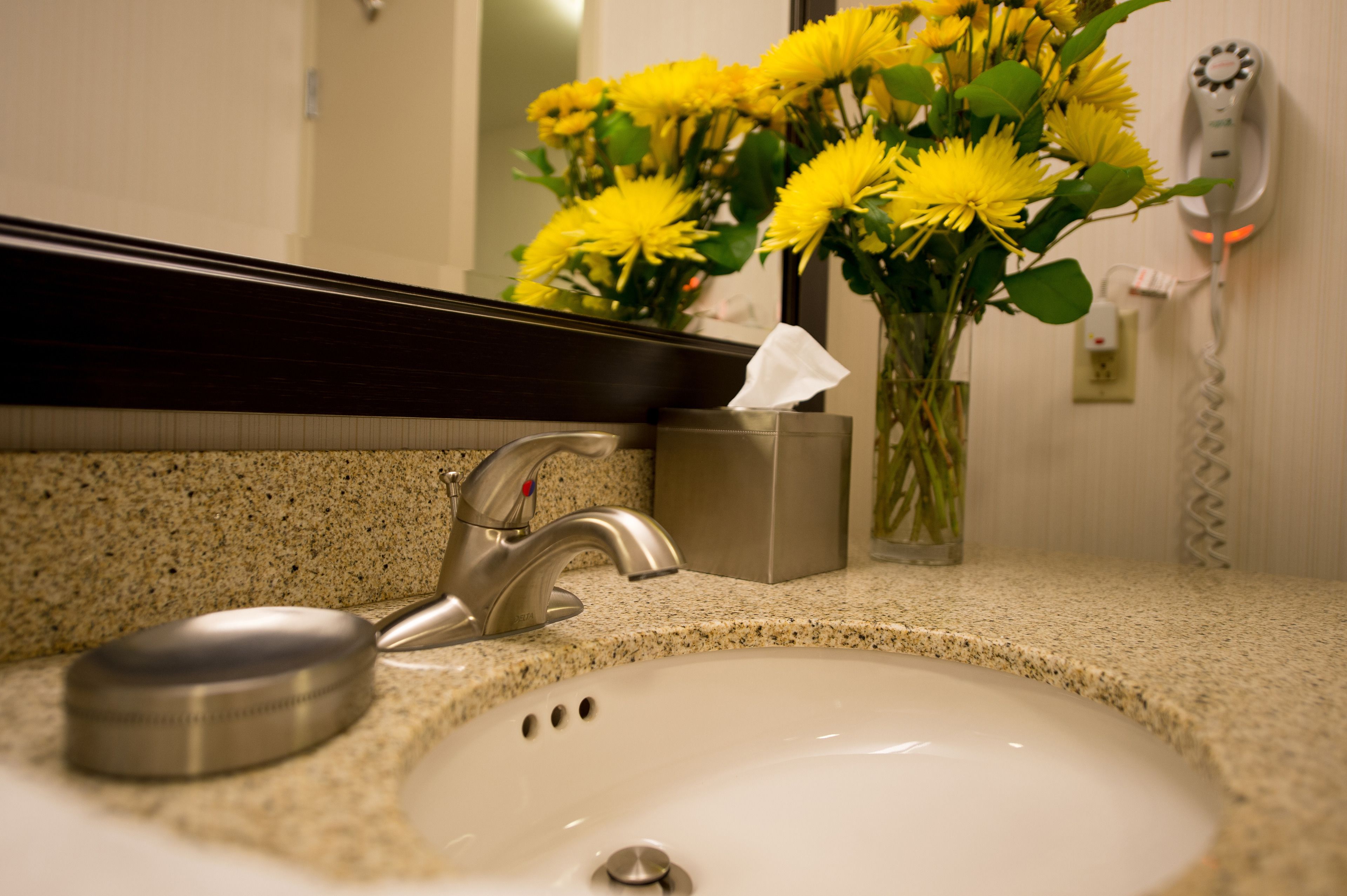 A bathroom sink with a faucet, a tissue box, and a vase with yellow flowers.