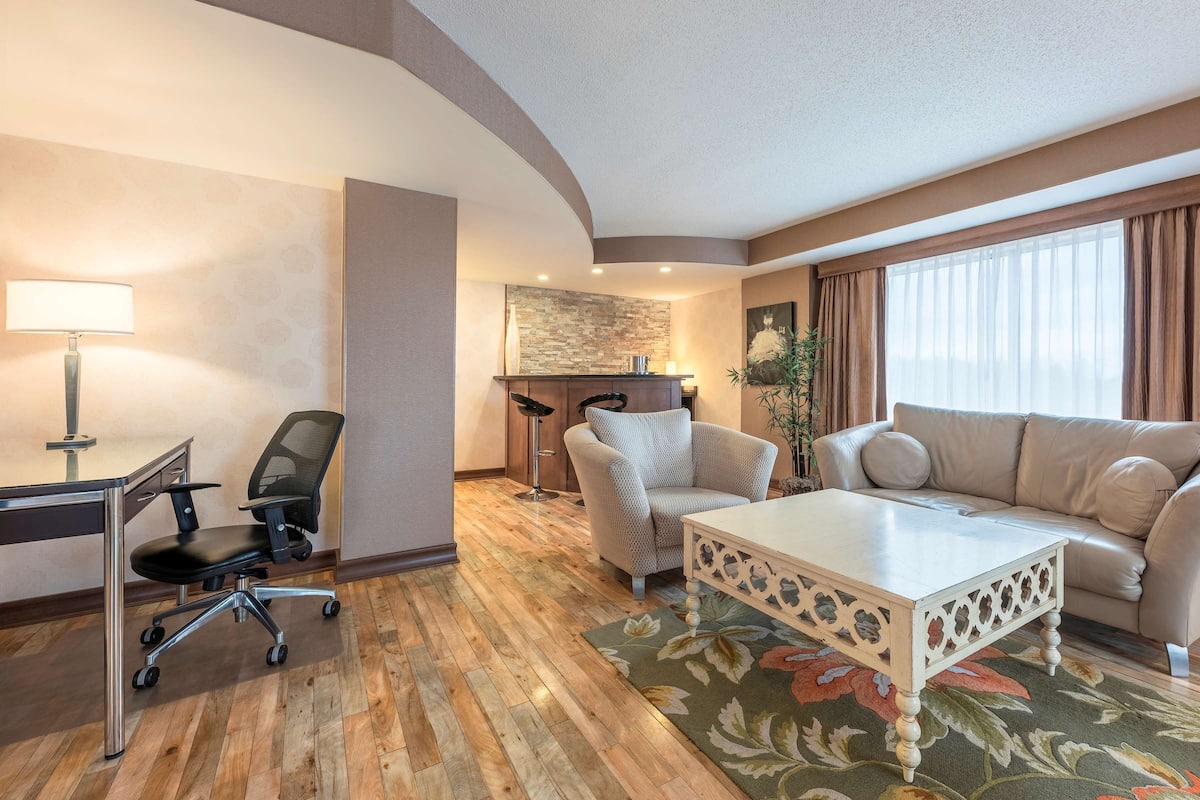 A hotel room with a desk, office chair, sofa, and a coffee table.