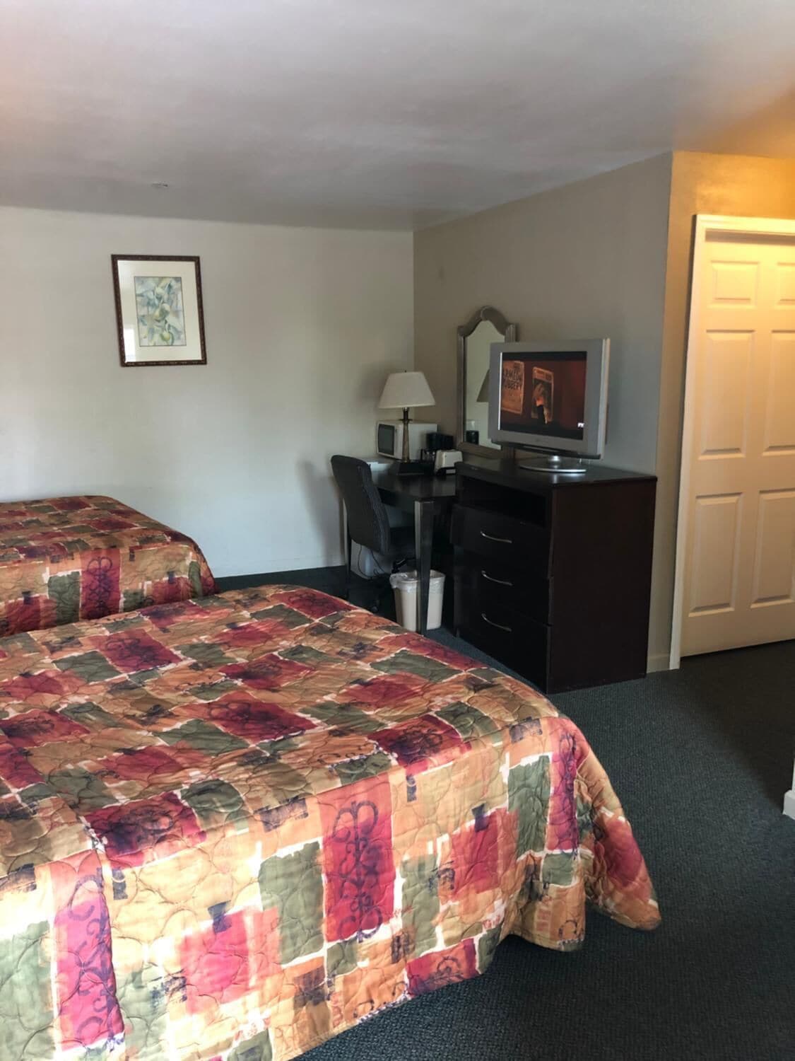 Habitación de hotel con dos camas, un escritorio con computadora, un televisor y una puerta.