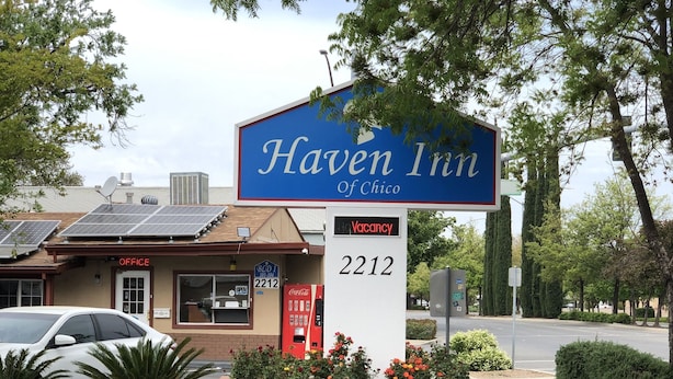Letrero del Haven Inn con cartel de habitaciones disponibles, una máquina expendedora de Coca-Cola y un coche aparcado.