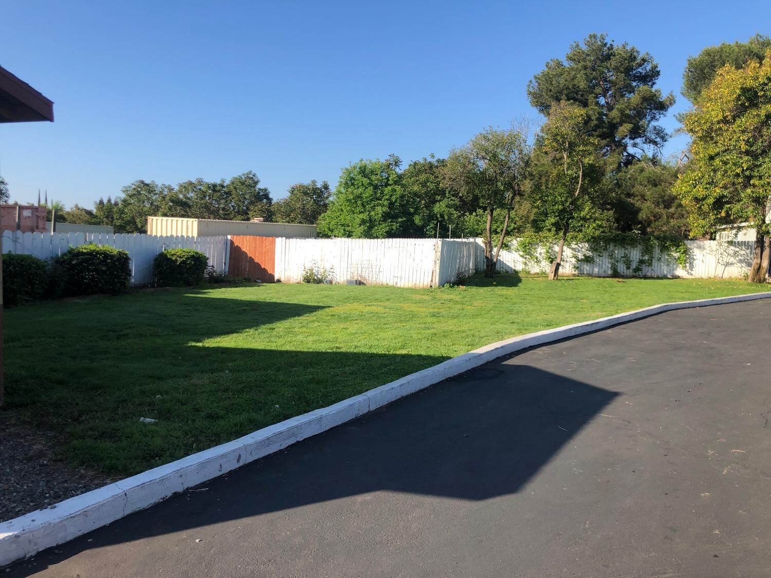 A parking lot with a green lawn and a white fence.