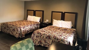 Una habitación de hotel con dos camas, cada una con una colcha estampada de flores y cabeceros a juego. Hay una pequeña mesa y una silla en la habitación.
