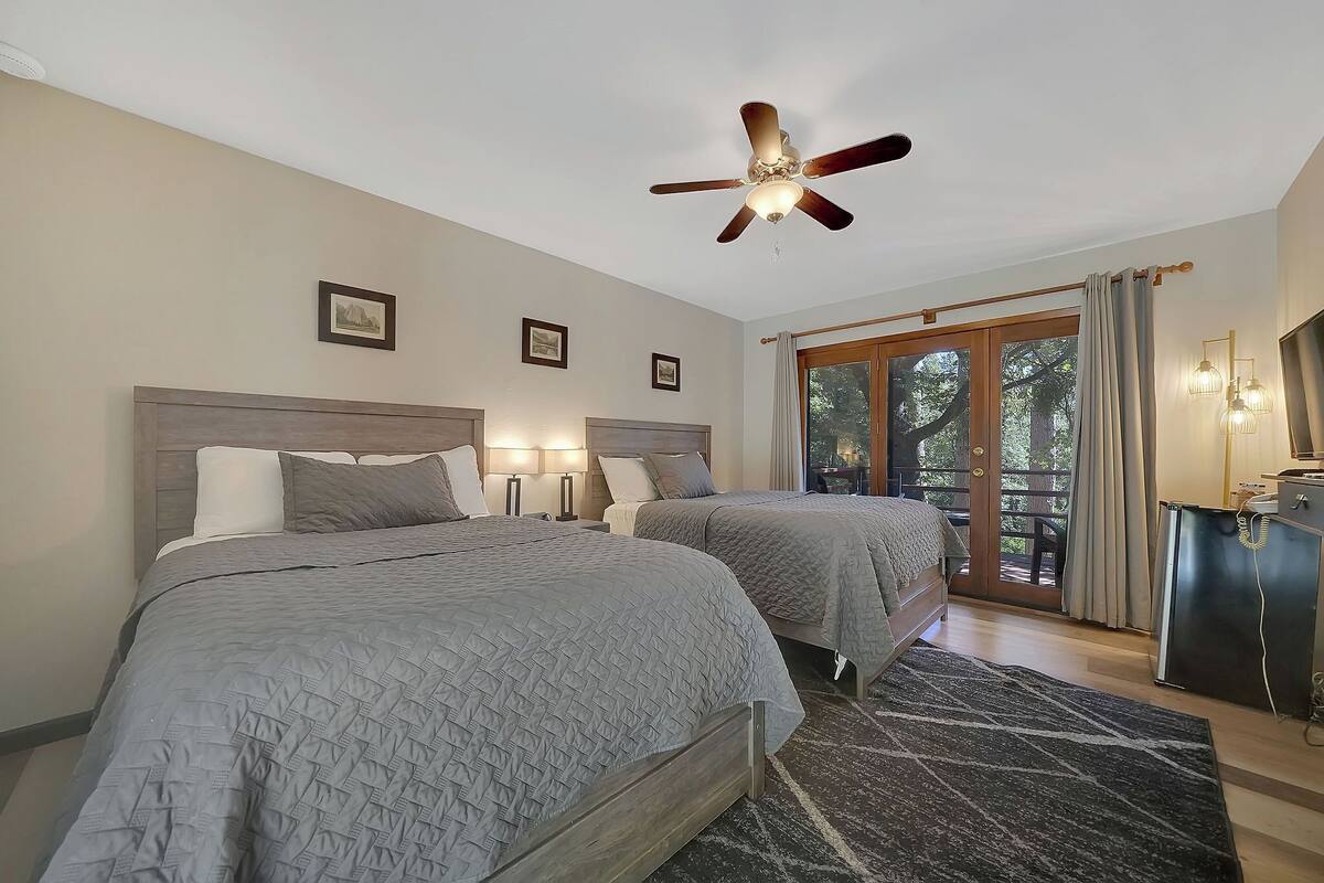 A bedroom with two beds, a ceiling fan, and a view of the outdoors through a sliding glass door.