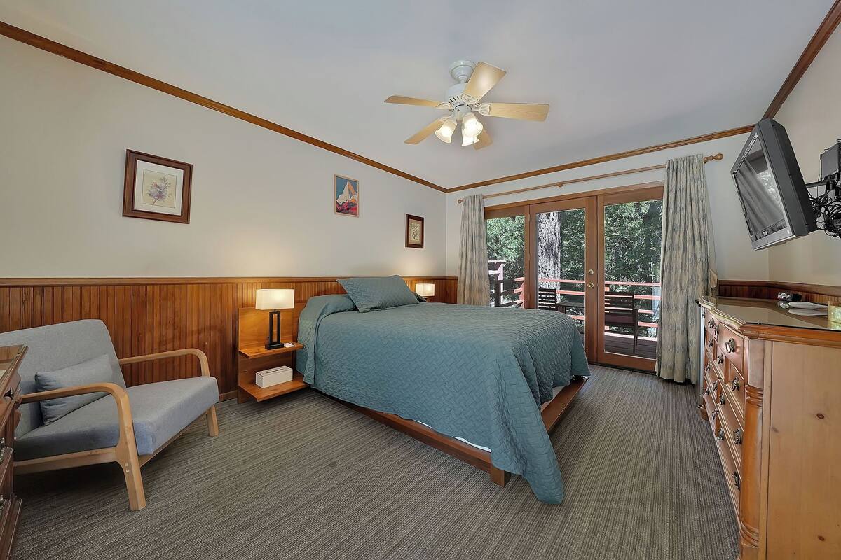 A bedroom with a bed, a chair, a nightstand, a dresser, a ceiling fan, and a window with a view of the outdoors.