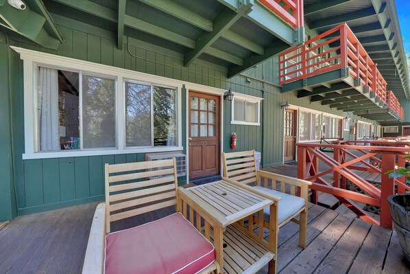 A wooden deck with a table and chairs, a wooden door, and a red railing.