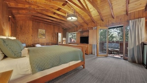 Ein Schlafzimmer einer Holzhütte mit Bett, Fernseher und einer Schiebetür zu einem Außenbereich.