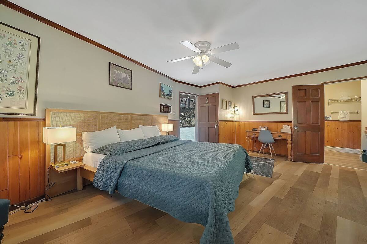 A bedroom with a bed, bedside lamps, a ceiling fan, and a desk with a chair.