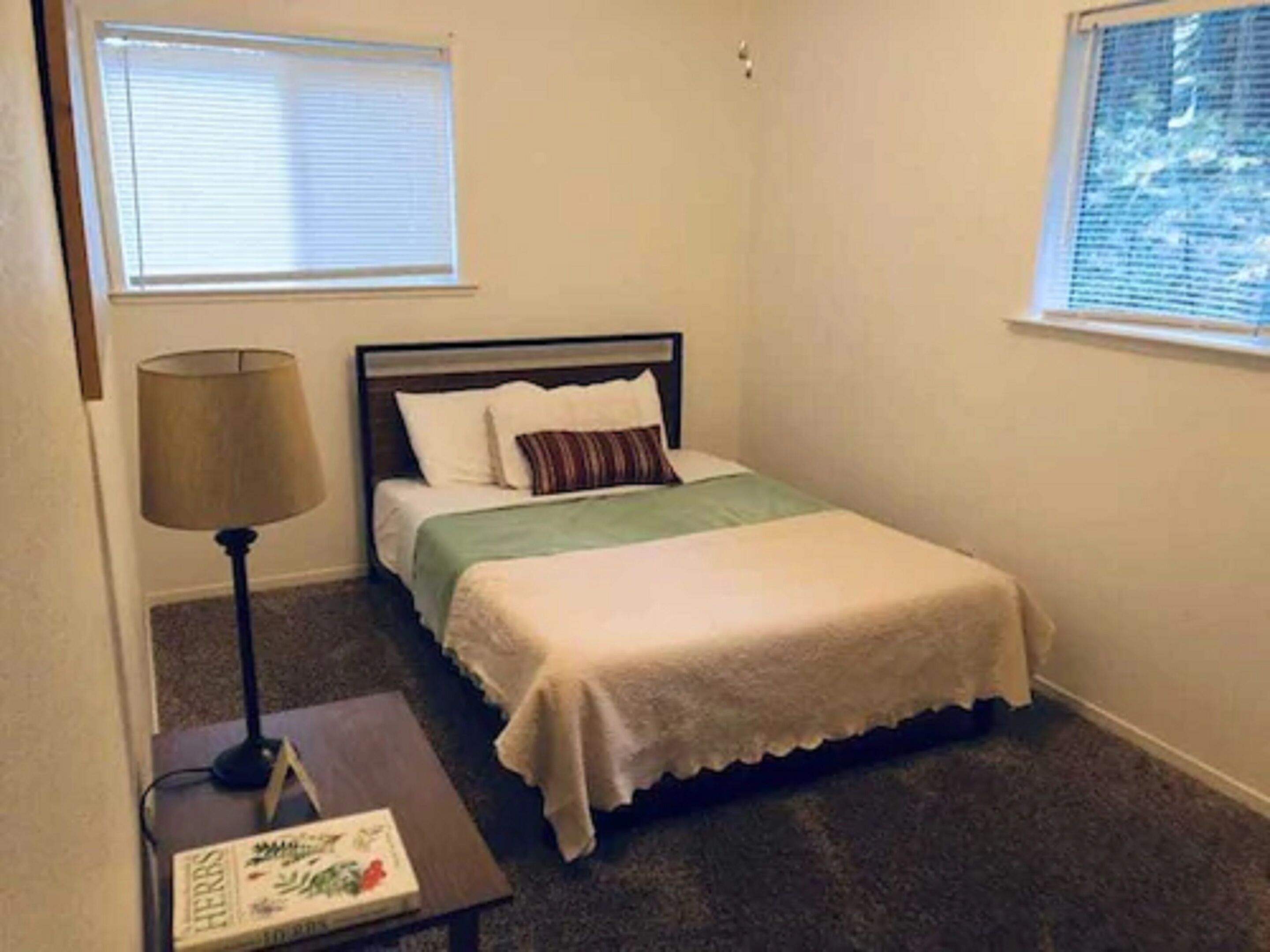 A bedroom with a bed, a nightstand, a lamp, and a window.