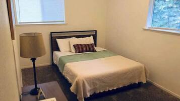 A bedroom with a bed, a nightstand, a lamp, and a window.