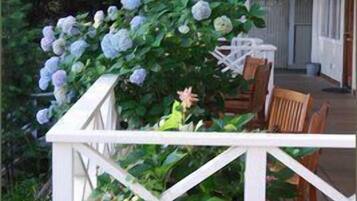 A wooden deck with white railings, surrounded by lush greenery and a flowering plant.