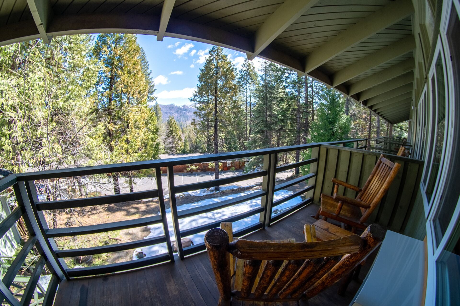 A wooden deck with a railing overlooking a forested area and a road.
