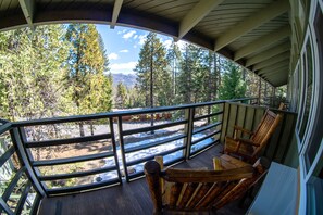 A wooden deck with a railing overlooking a forested area and a road.