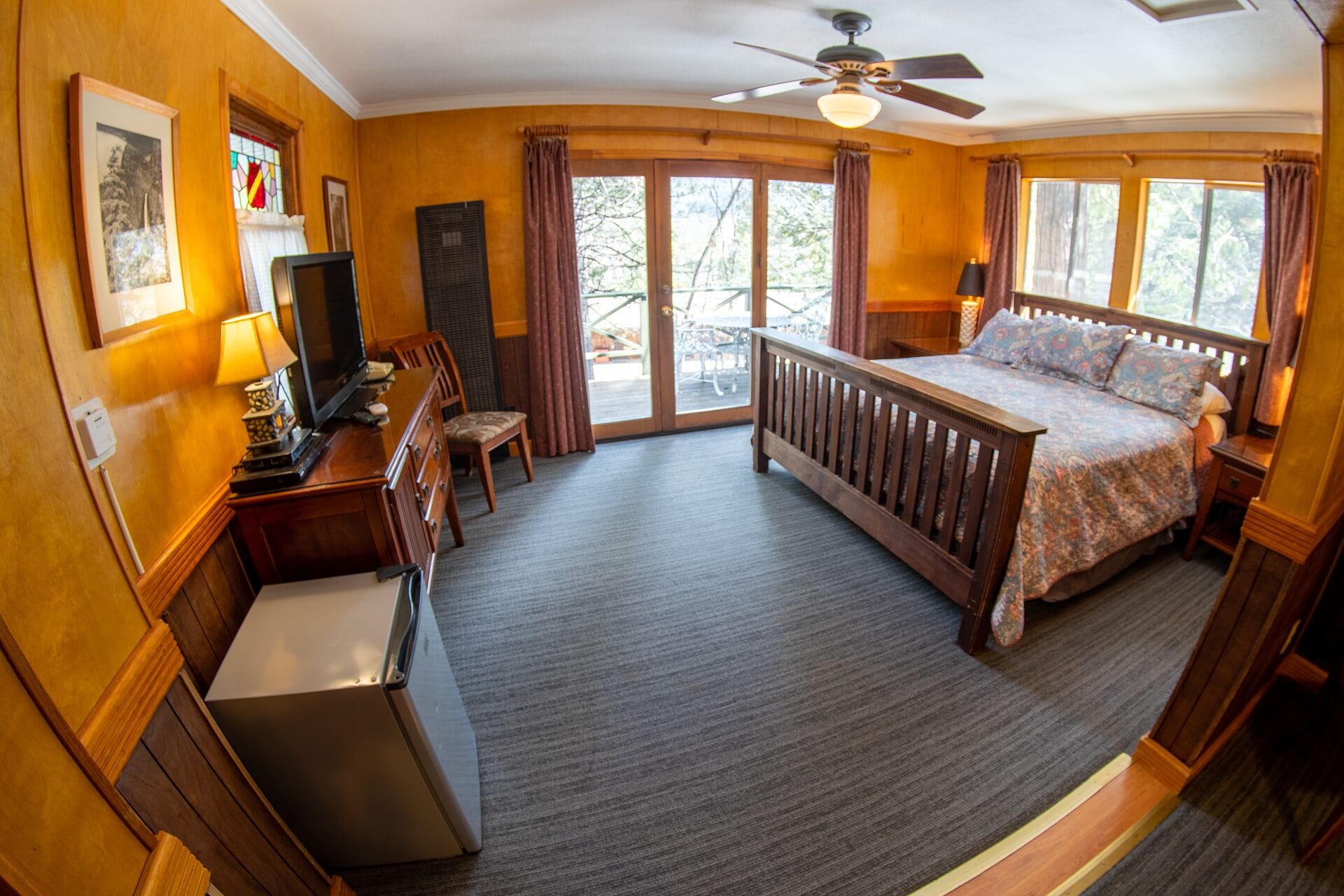 A hotel room with a bed, a desk, a television, a chair, and a balcony with curtains.