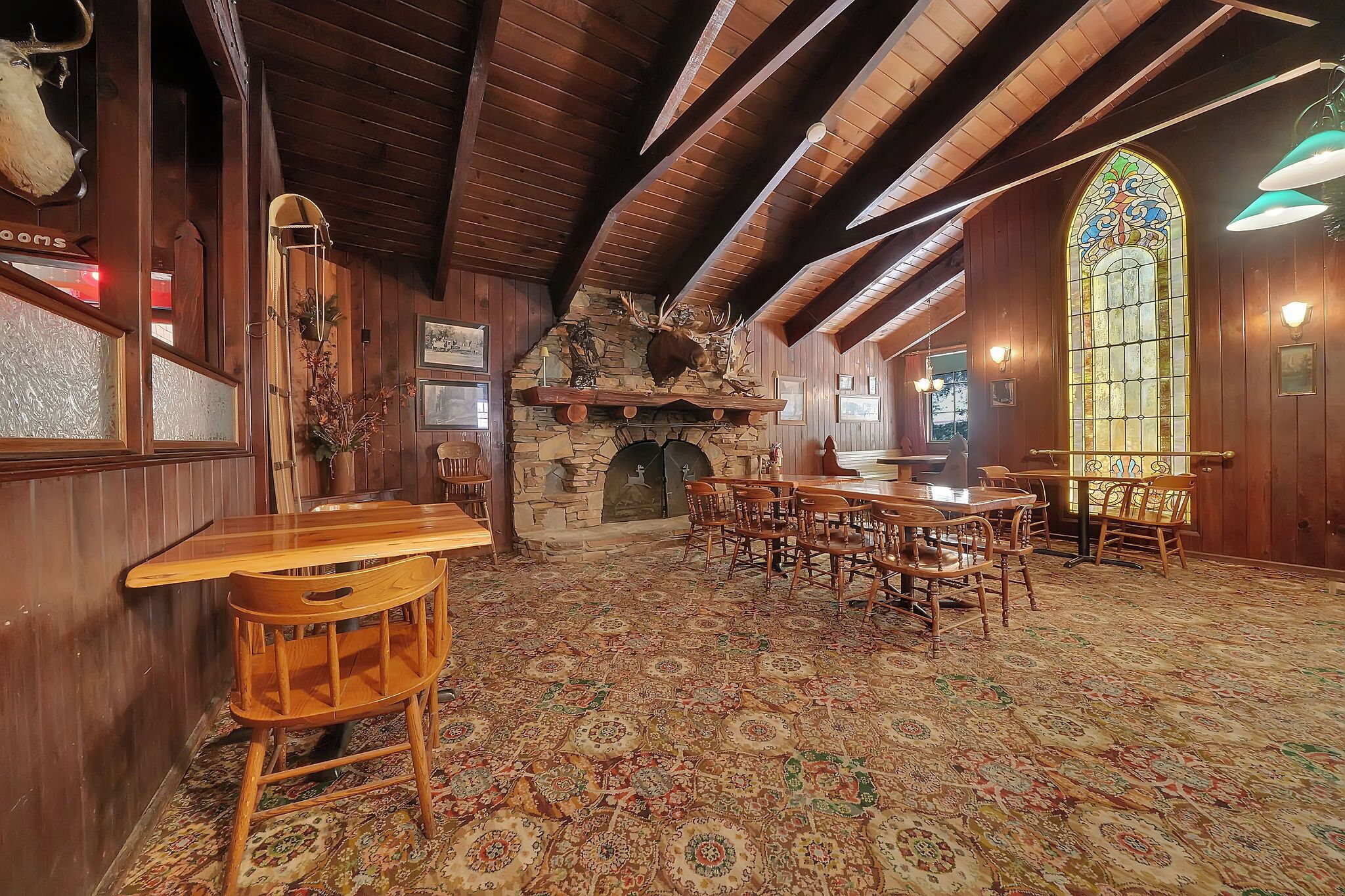 A rustic interior with wooden walls, a stone fireplace, and a patterned carpet.