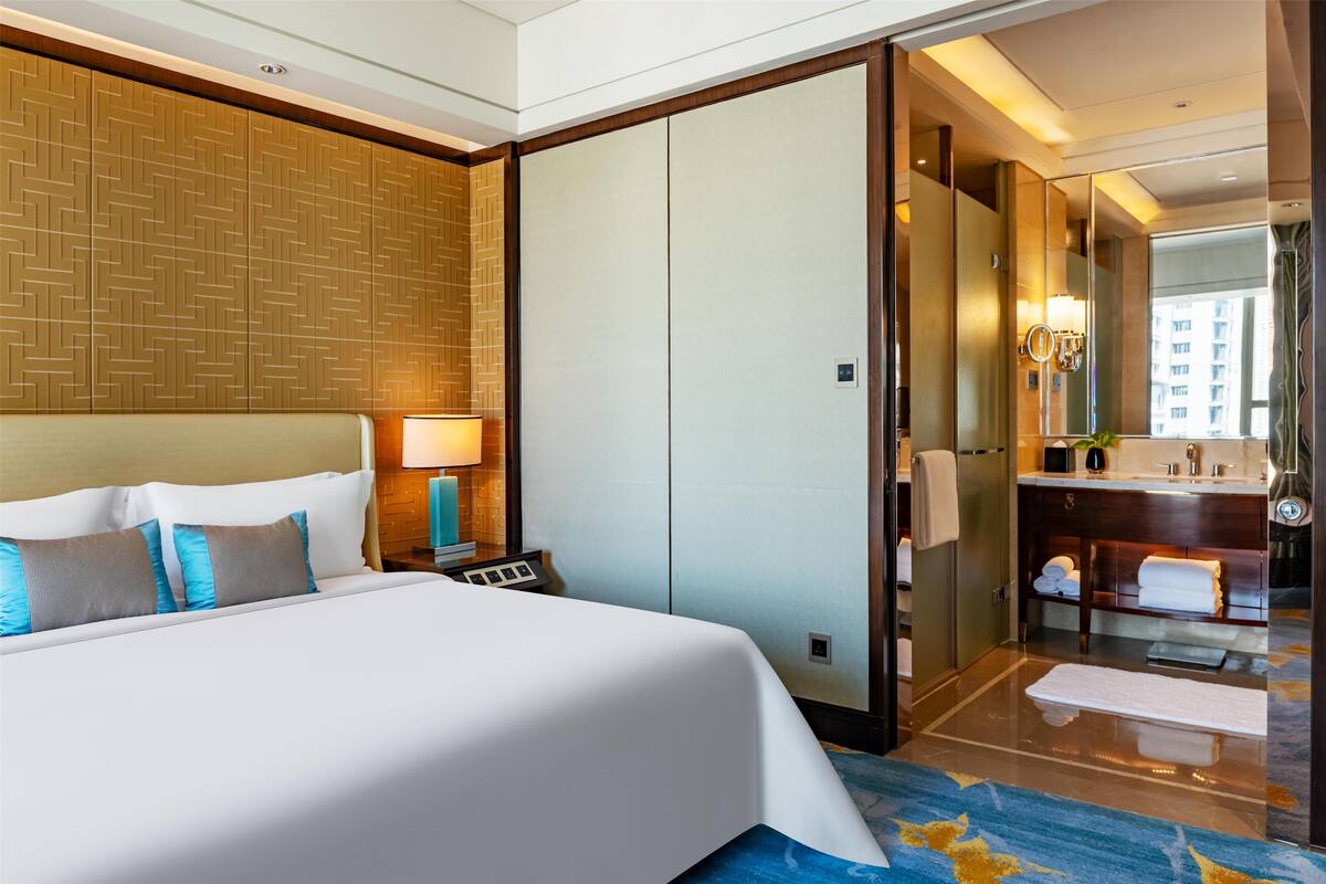 A hotel room with a large bed, a nightstand, a mirror, a bathroom with a sink and towel rack.