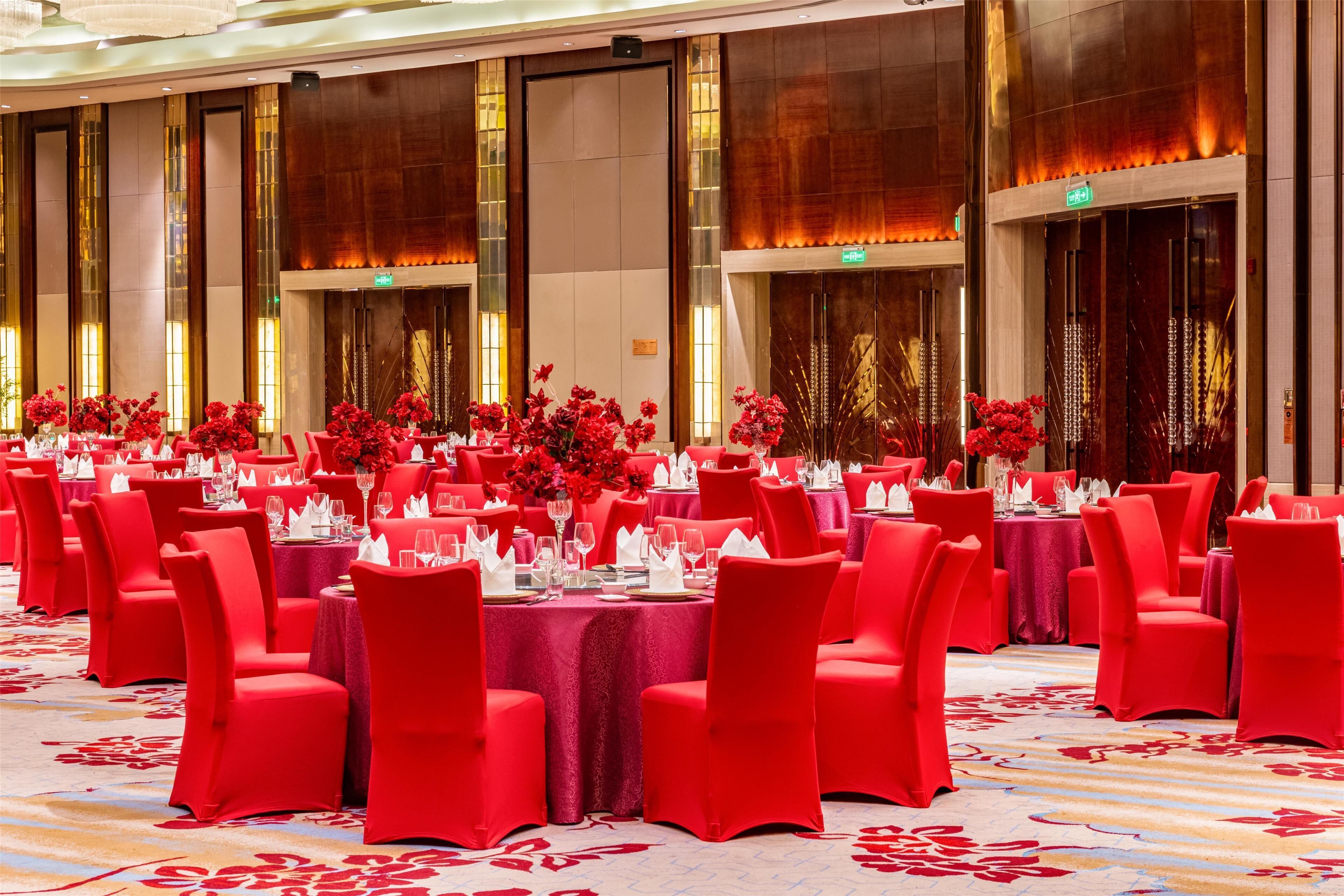 A banquet hall with round tables set for a formal event, featuring red chairs and floral centerpieces.