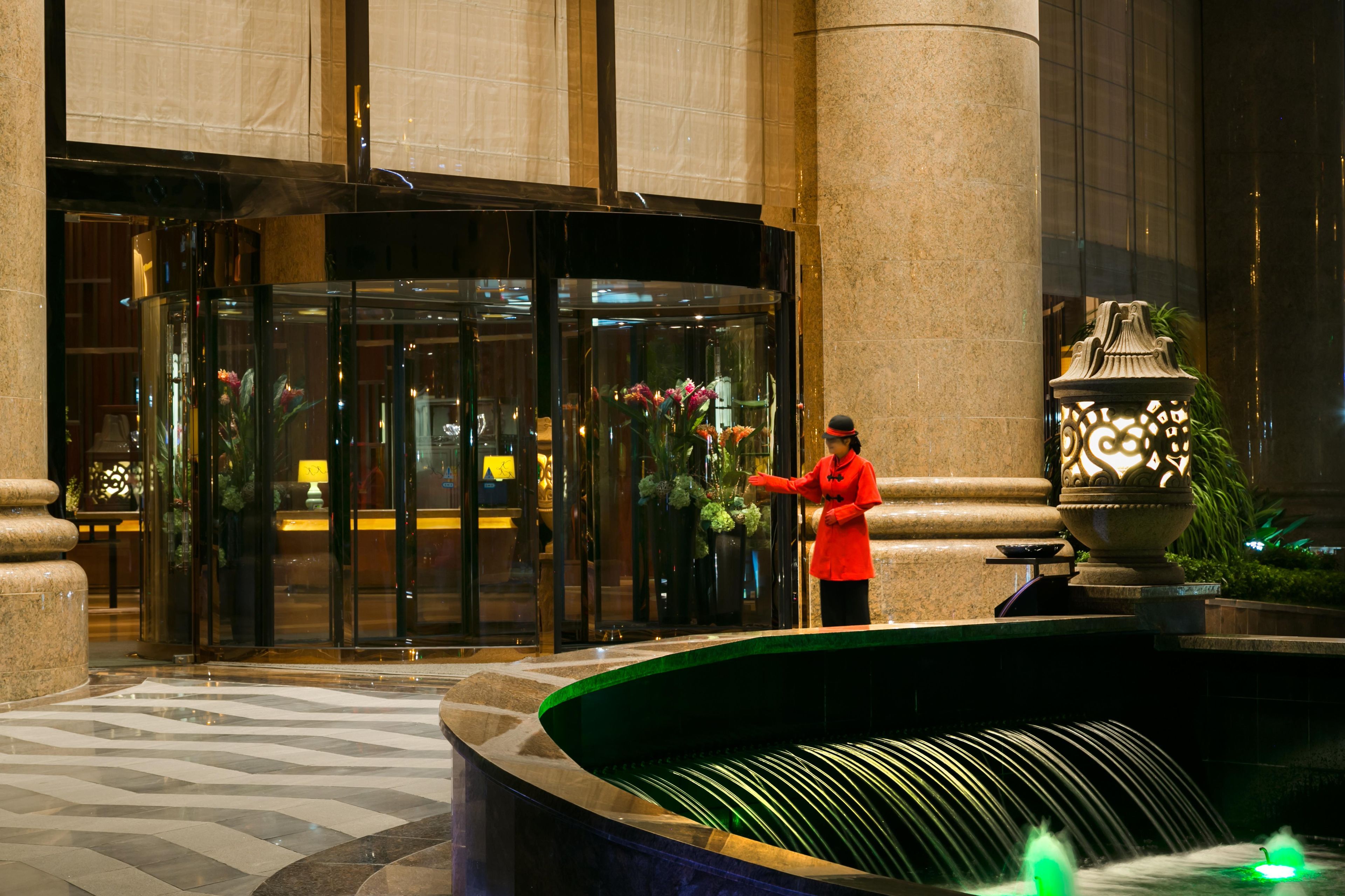 A hotel entrance with a revolving door, a fountain, and a reception area with a receptionist.
