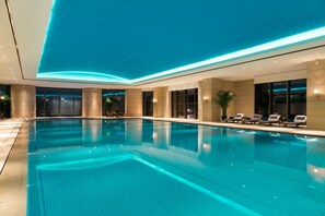 A large indoor swimming pool with a starry ceiling, lounge chairs, and a view of the city at night. - Kempinski Hotel Xiamen (Xiamen)