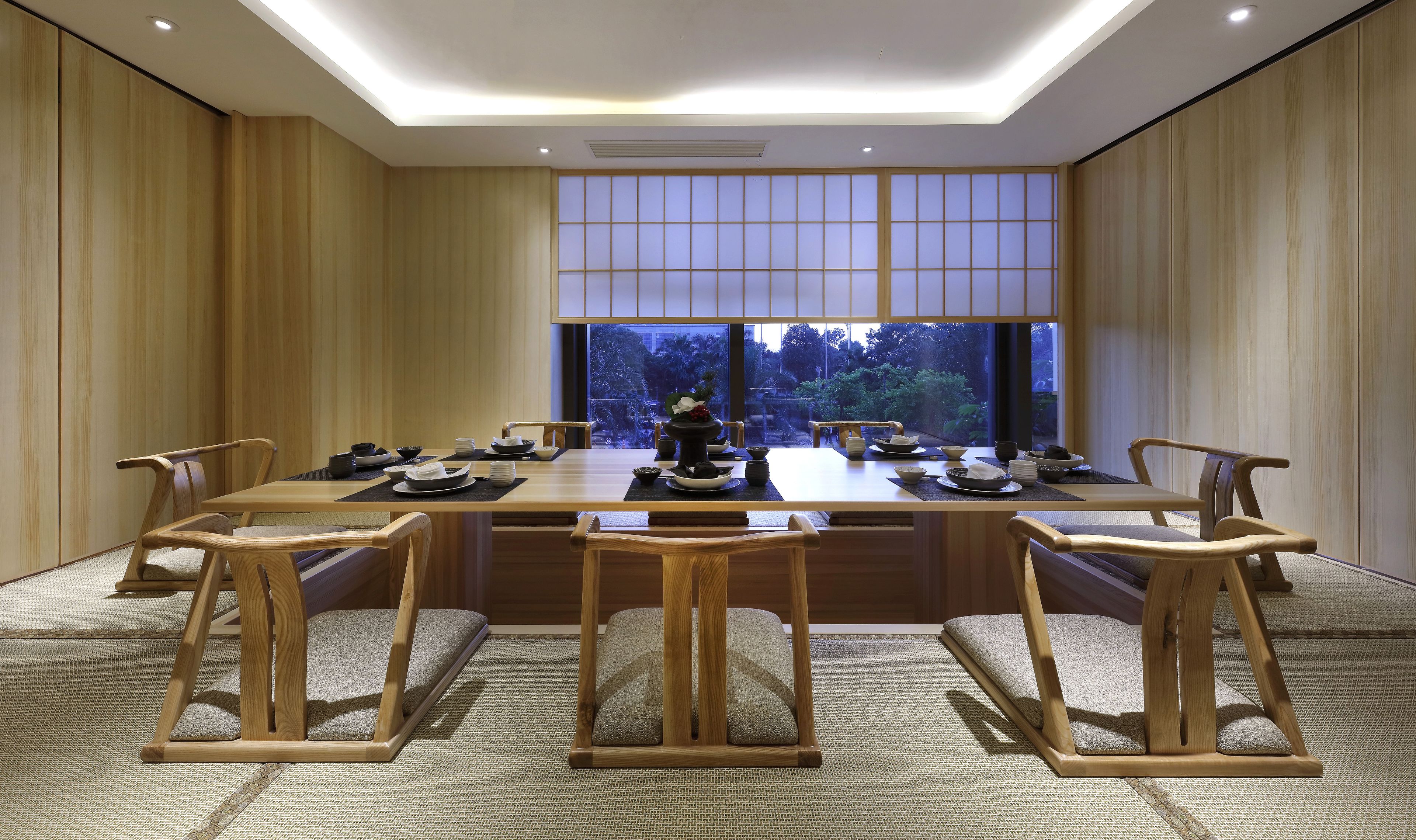A traditional Japanese-style dining room with a low table set for six, surrounded by wooden chairs.