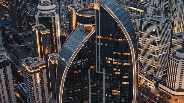 Un moderno edificio de gran altura con fachada de vidrio curvada, rodeado de otros edificios altos en un paisaje urbano.