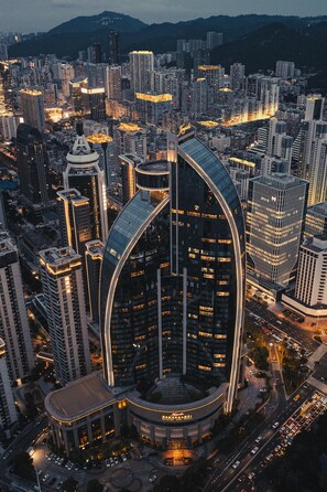 Un moderno edificio de gran altura con fachada de vidrio curvada, rodeado de otros edificios altos en un paisaje urbano.