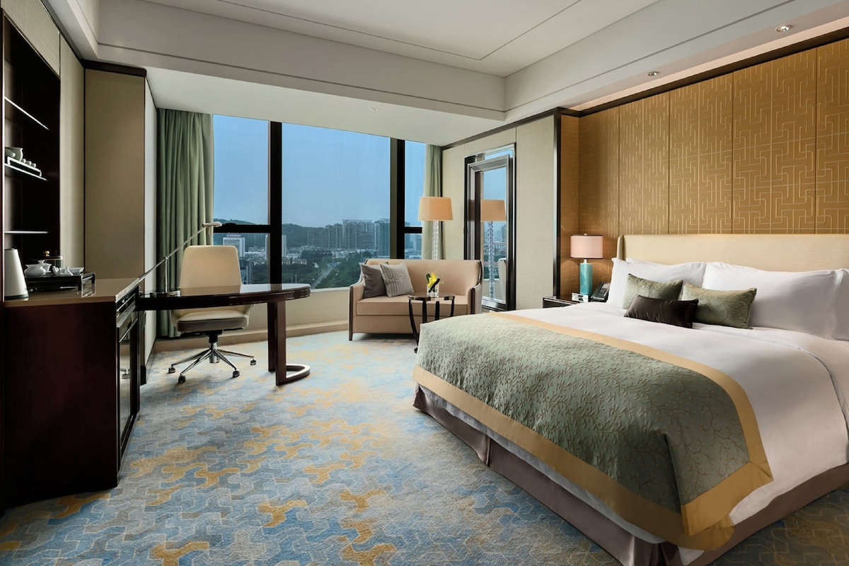 Habitación de hotel con una cama grande, un escritorio, una silla y vistas a la ciudad.