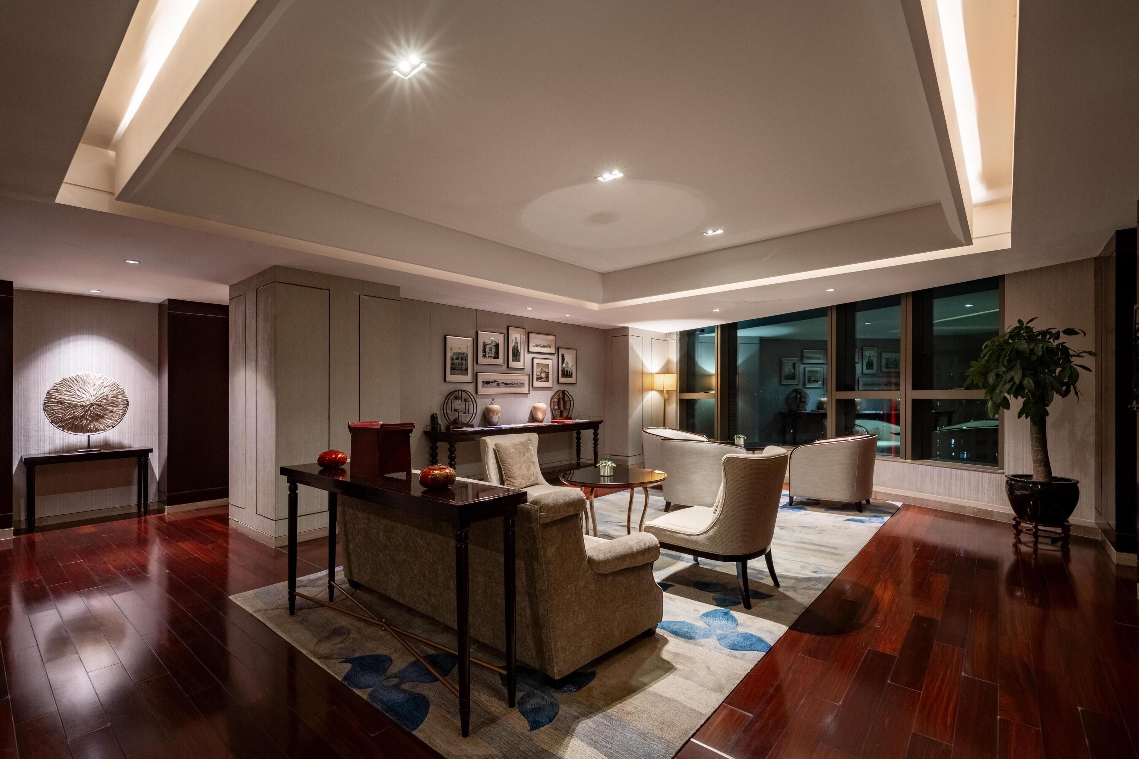 Uma sala de estar moderna com sofá, poltronas, mesa de centro e mesa de jantar. Há quadros nas paredes, um abajur e um vaso de planta.