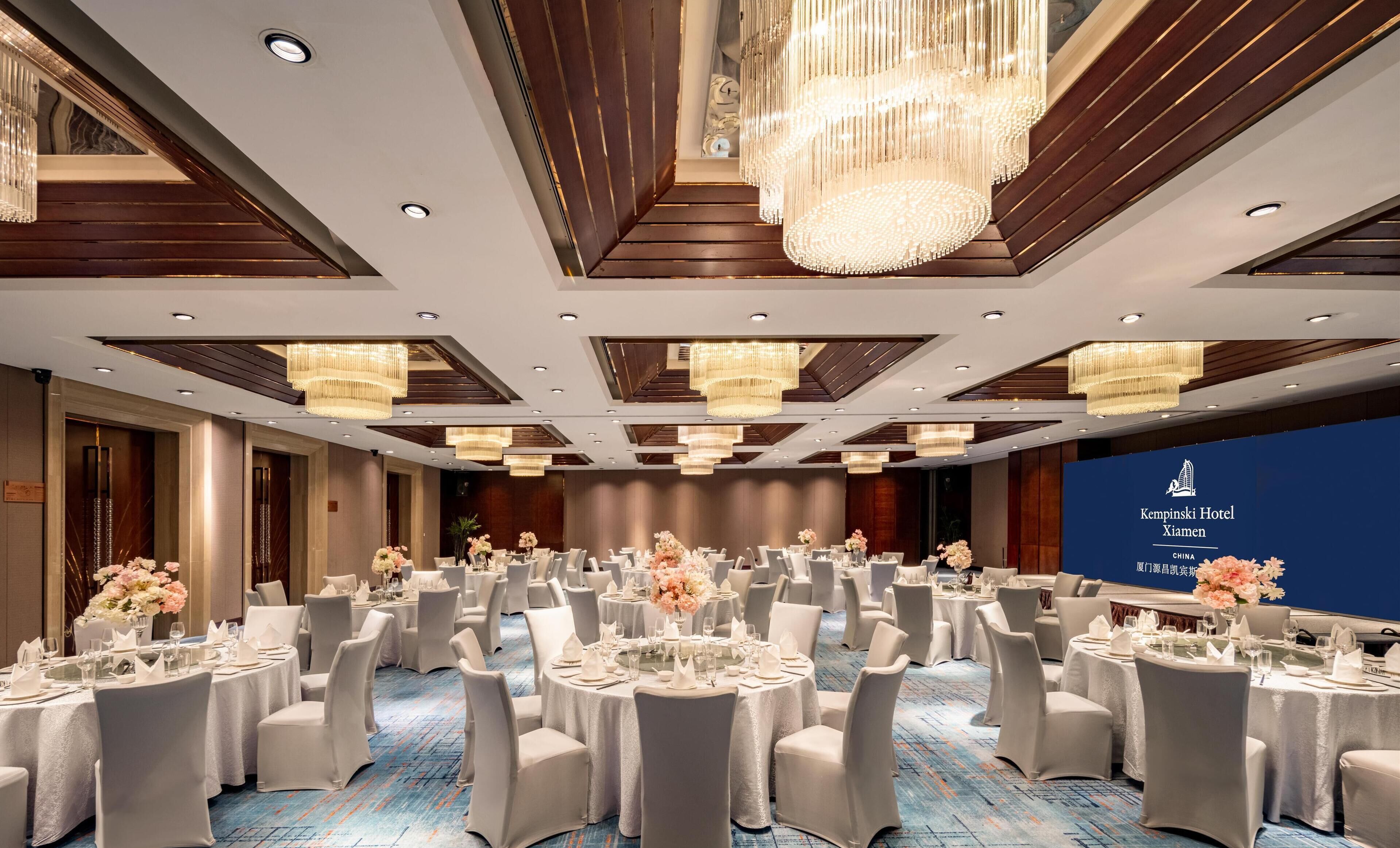 A large banquet hall with round tables, white tablecloths, and floral centerpieces.
