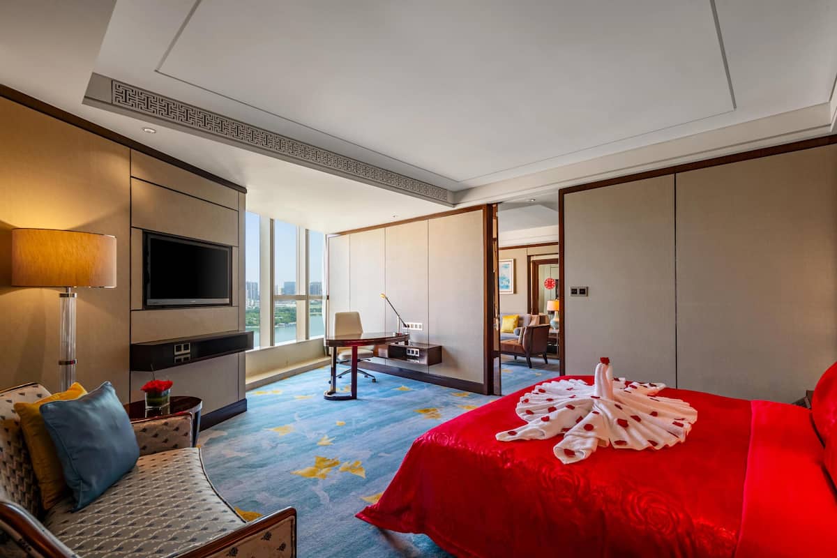 A hotel room with a large bed, a TV, a desk, and a view of the city.