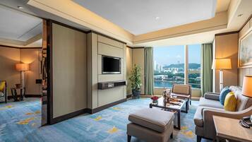 A hotel room with a large TV, comfortable seating, a view of the city, and a blue carpet with yellow patterns.