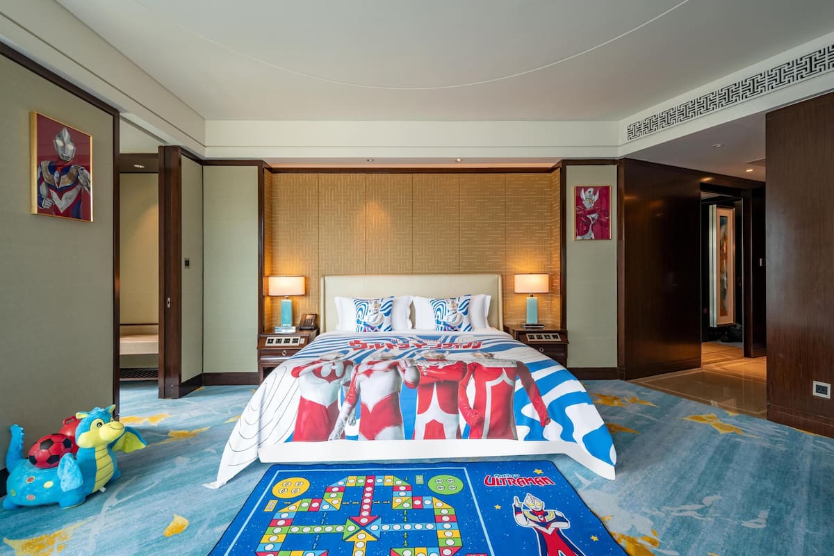 A hotel room with a large bed, two bedside tables, a nightstand, a wall-mounted TV, and a carpet with a colorful design.