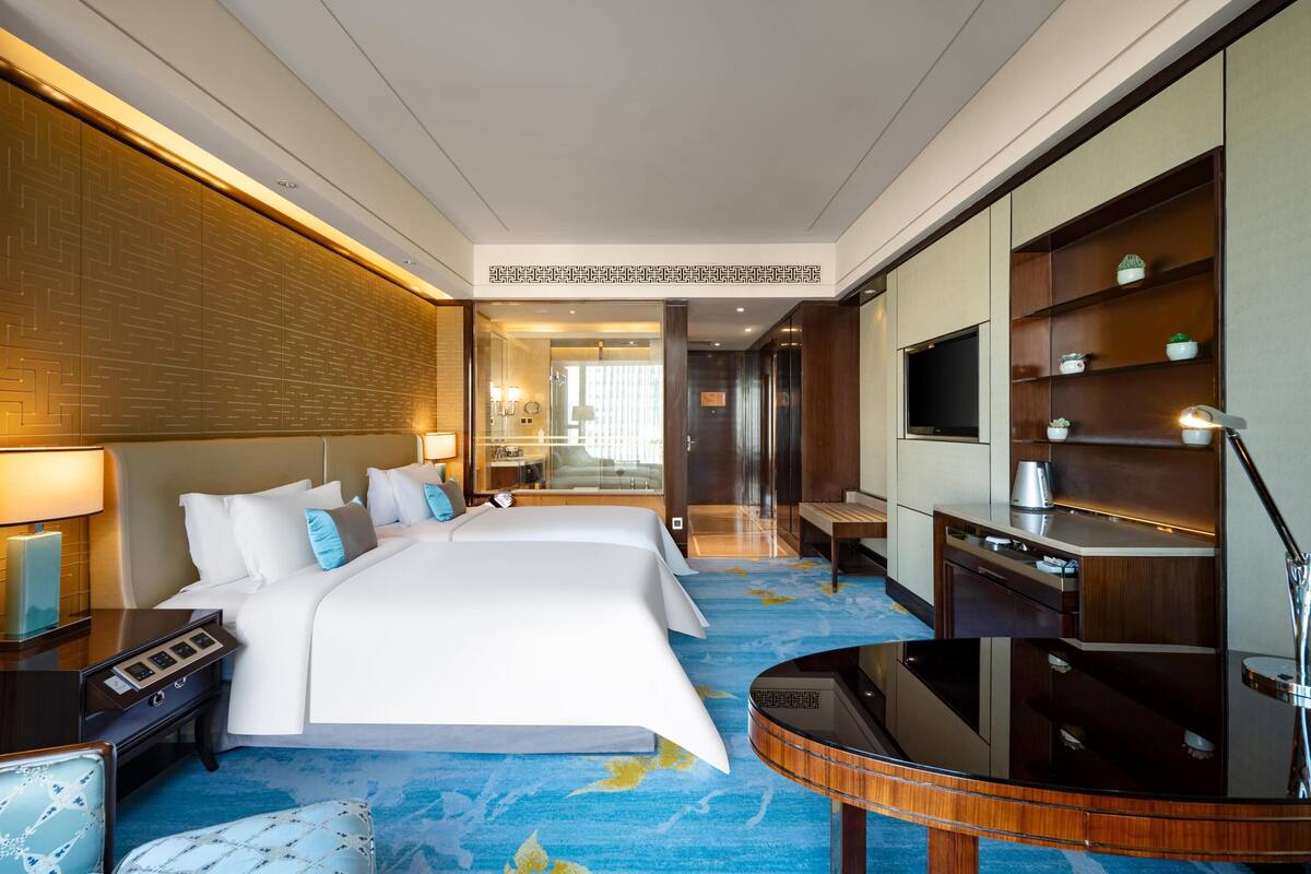 A hotel room with a large bed, a desk, a TV, and a minibar.
