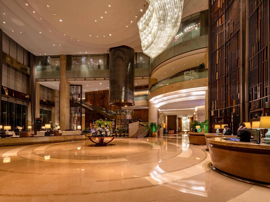 A spacious lobby with a central reception desk, multiple seating areas, and a large chandelier.