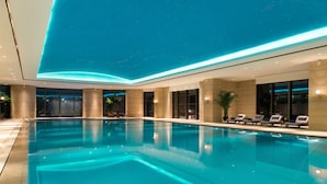 Una amplia piscina cubierta con agua cristalina y azul, rodeada de sillones de descanso y un techo con estrellas.