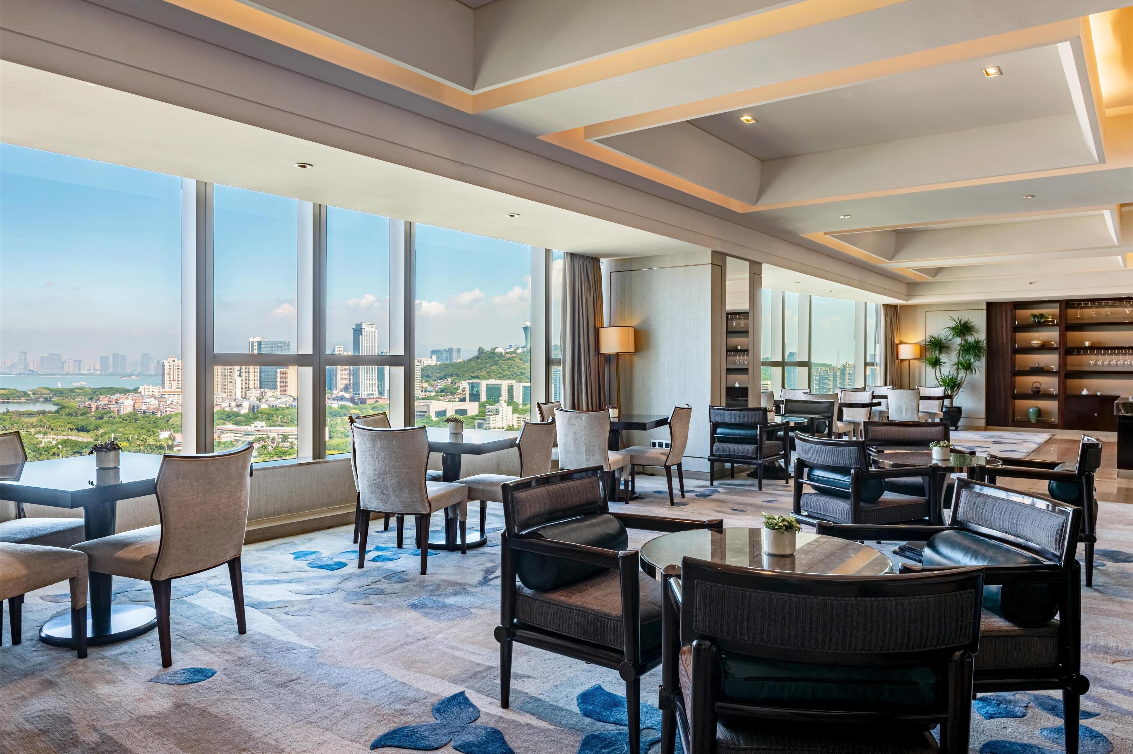 A spacious hotel lobby with large windows offering a city view, comfortable seating areas, and a well-lit interior.