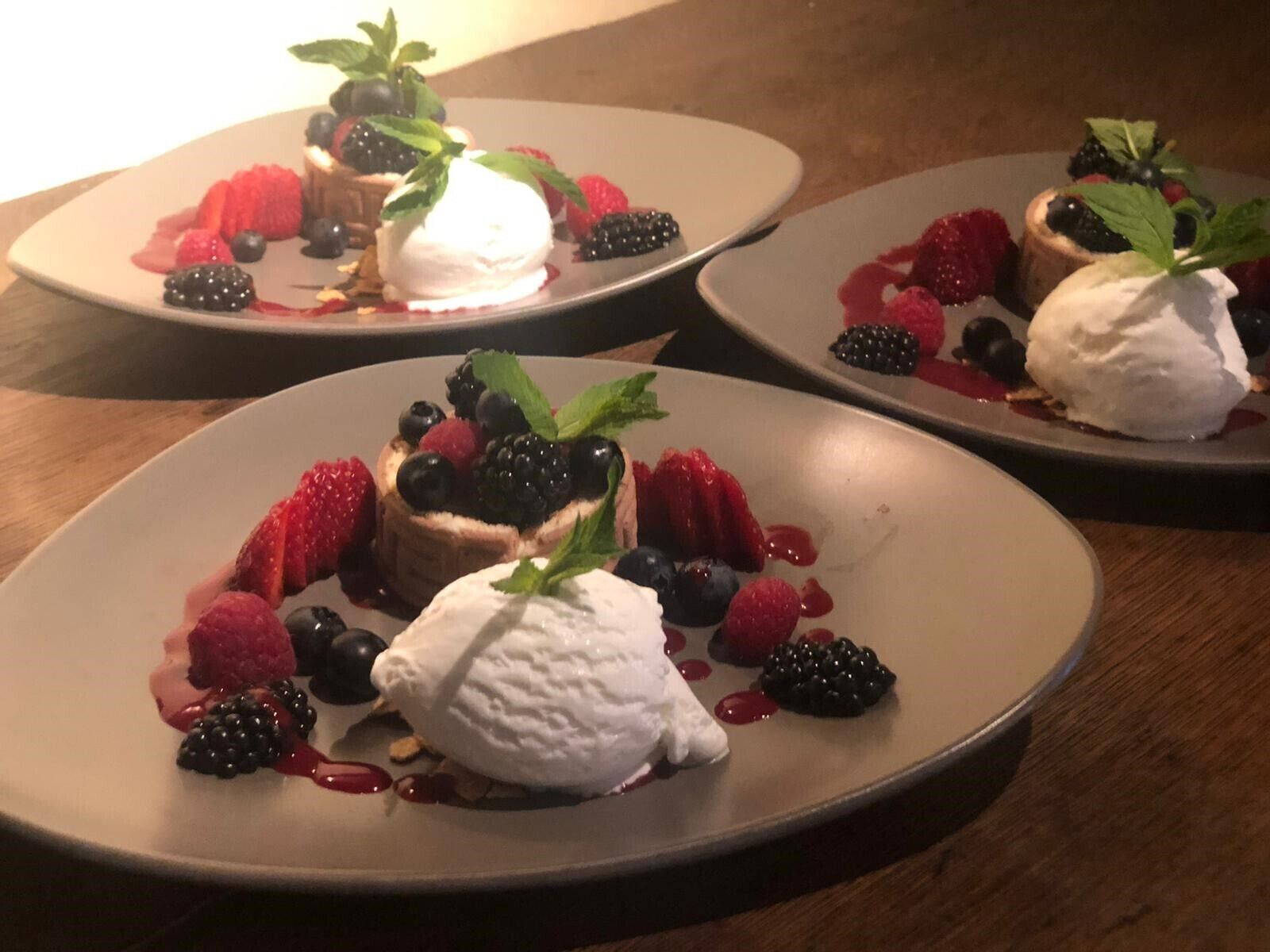 Three plates of dessert with berries and whipped cream.