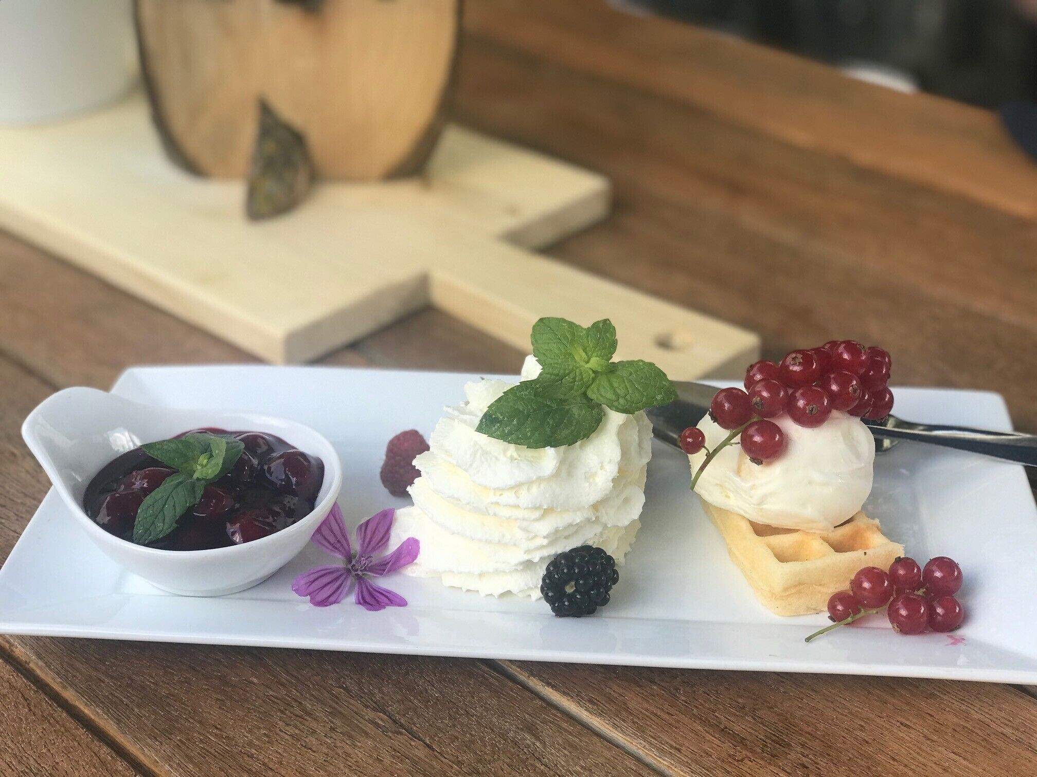 Une assiette à dessert garnie de crème fouettée, de fruits rouges et d’un petit bol de compote de fruits rouges.