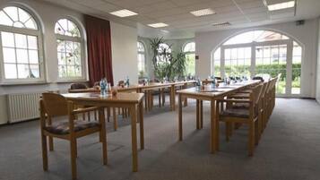 A conference room with multiple tables and chairs, large windows, and a view of greenery outside.