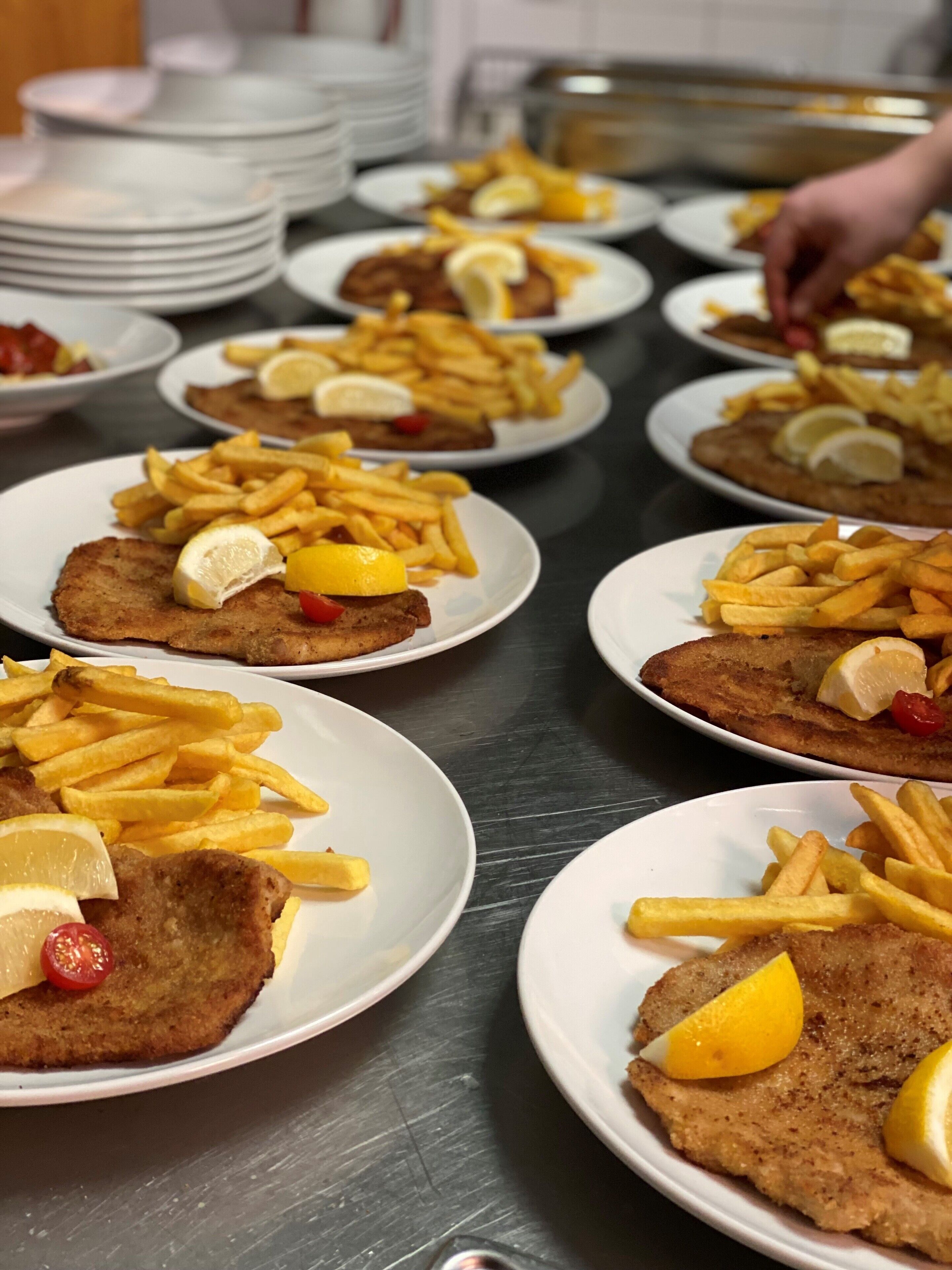A buffet table with plates of food, including breaded cutlets and fries, arranged on a stainless steel table.